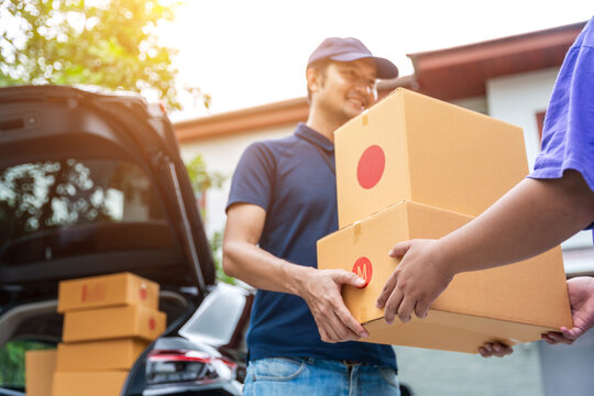 Asian delivery man in uniform holding a cardboard box, smiling as he delivers a package to a customer
