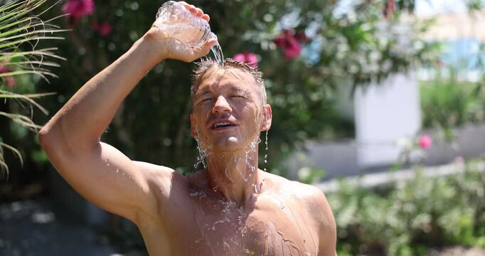 Handsome man douses himself with cold water from bottle in summer. Sultry heat in summer and cool shower concept