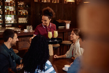 Happy waitress serving drinks to group of friends in  bar.
