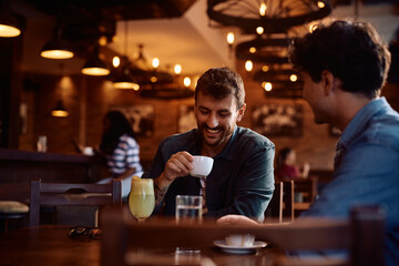 Happy man having  cup of coffee while being with  friend in  café.