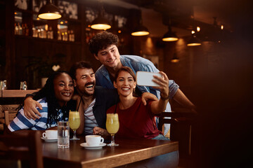 Group of happy friends taking selfie while gathering in  café.