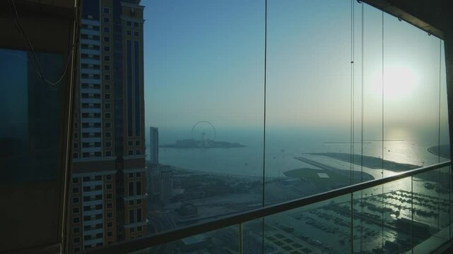 View of Bluewaters Dubai through a window from the Dubai Marina complex. The setting sun in the frame.