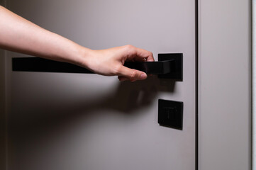 Naklejka premium An unrecognizable woman reaches out with her hand to a modern door and a black door handle to open the room