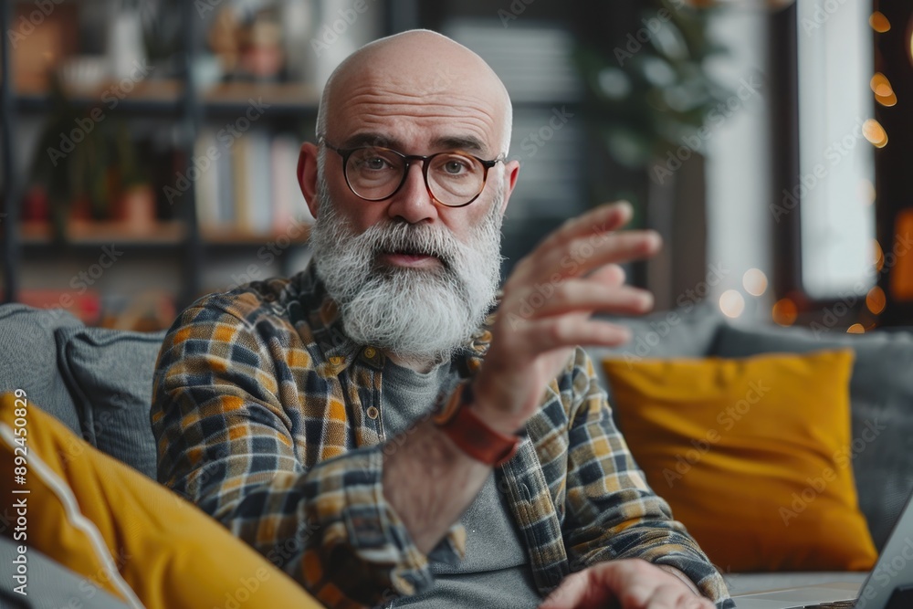 Poster a man with a beard and glasses is sitting on a couch with a laptop in front of him. he is talking to