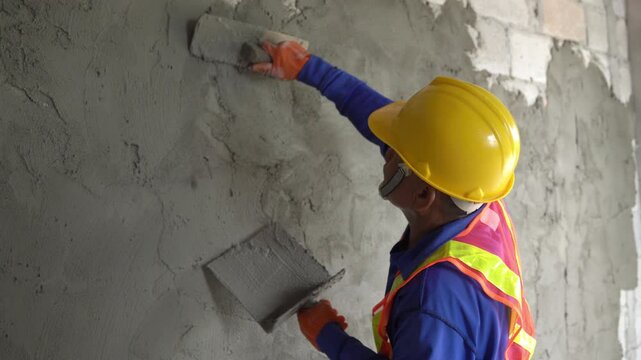 A construction worker carefully plastering a wall with cement, ensuring a smooth and even finish in a new house.