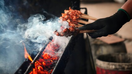 Satay ayam or sate ayam is Indonesian food and cuisine of seasoned, skewered and grilled chicken with palm stick served with peanut, soy and chili sauce.Serving on wooden table and brown food burner