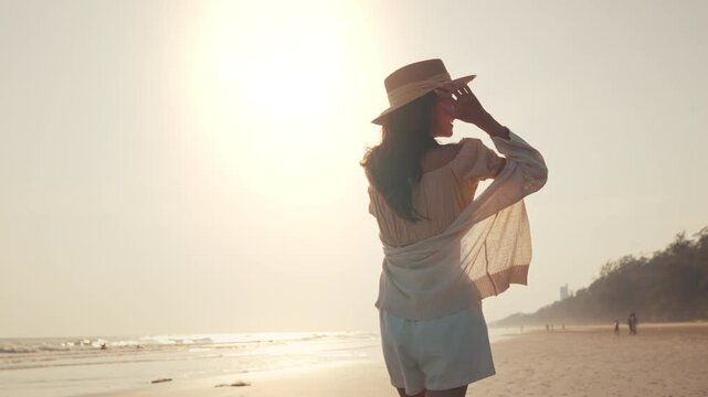 Slow motion side view of young asian woman with freedom on the sea beach at golden sunset, Female tourist on seaside summer vacation.