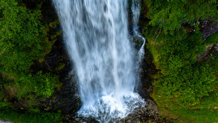 waterfall cascades down a rocky cliff face in Norway, creating a swirling mist at its base. Lush green vegetation surrounds the falls, Fjaerlandsfjorden, Fjord, Vestland, Norway