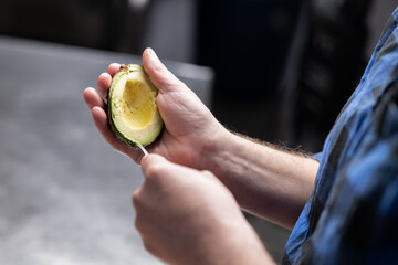 Person's hands holding avocado half and scooping out flesh with spoon