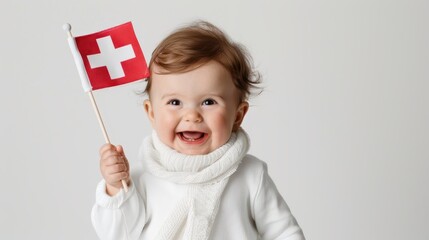 An adorable baby dressed in white holding a small Swiss flag, smiling joyfully while wearing a white scarf. The baby's excitement is palpable in this charming portrait.
