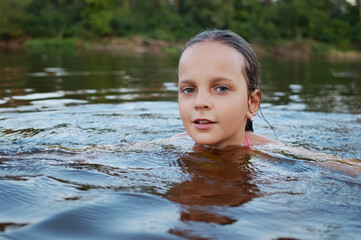 Fototapeta premium Charming Caucasian little girl swimming in river excited child having wonderful rest at beach and savoring summer vacation and holiday while relaxing in water looking at camera