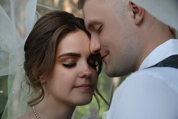portrait of happy bride and groom under white veil outdoors, marriage ceremony