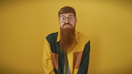 Bearded redhead man with glasses posing over a yellow background, exuding a quirky charm