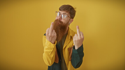 Handsome redhead bearded man in glasses showing middle fingers against a vibrant yellow background,...