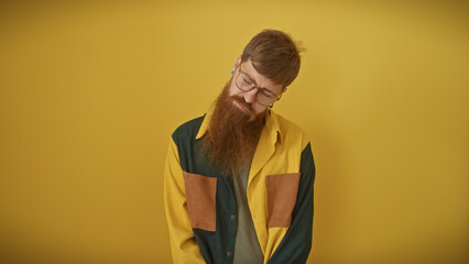 A pensive redhead man with a beard, glasses, and a colorful shirt stands against a yellow background.