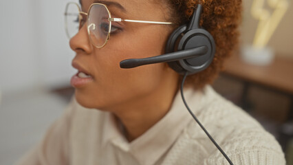 African american woman wearing headset working from home with a neutral interior background