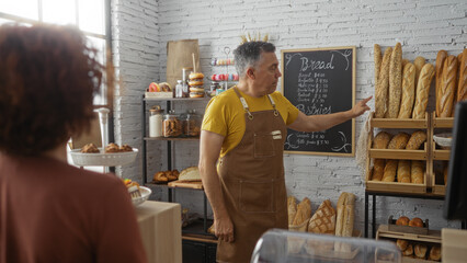 Man baker explaining bread selection to woman customer in cozy bakery shop interior