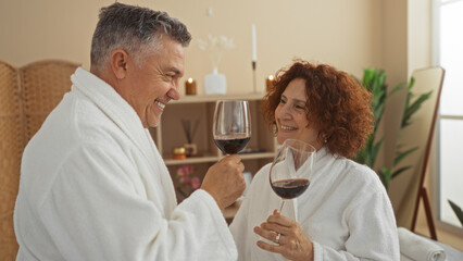 Middle-aged couple enjoying wine together in a spa wellness center wearing white bathrobes