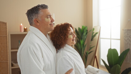 Fototapeta premium Middle-aged couple enjoying a serene moment with eye masks in a peaceful spa room, adorned with greenery and candles, showcasing relaxation, beauty, and wellness indoors together
