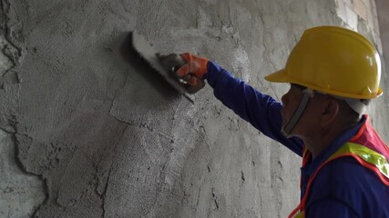 Asian construction worker carefully plastering a wall with cement at the construction site of an unfinished house.