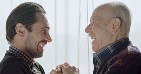 Middle-aged man and his father talking and then embracing in relief smiling, laughing and holding...