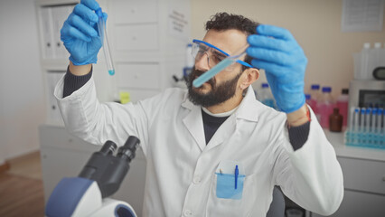 Naklejka premium A middle-aged bearded scientist in a white lab coat analyzing a blue liquid in a test tube inside a laboratory.