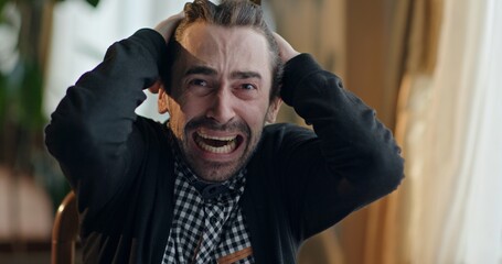 Distraught man reacting with grief while sitting on chair at home