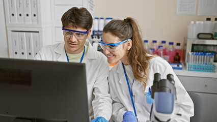 Two scientists, a woman and a man, collaborate in a laboratory, working on a laptop among scientific equipment.