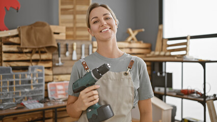 A confident young woman holds a drill in a well-organized carpentry workshop, embodying diy and craftsmanship.