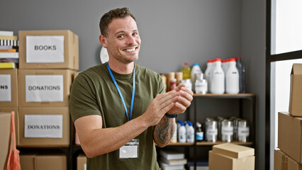 A cheerful young man applauding in a storeroom with labeled boxes and donations.