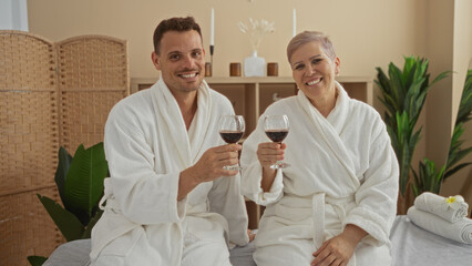Obraz premium Man and woman in spa robes enjoying wine together in indoor wellness center, embodying relaxation and contentment in a serene environment