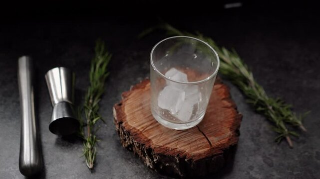 Ice cubes fall into a glass with lime and rosemary and topped with soda. The process of preparing a cocktail and a refreshing summer drink with alcohol for a party. Cold water with gin