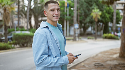 Handsome young hispanic man using smartphone on urban city street.