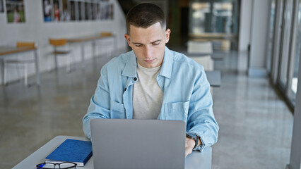 Focused hispanic man using laptop at university campus indoors.