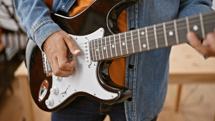 Hispanic man playing electric guitar in a music studio.