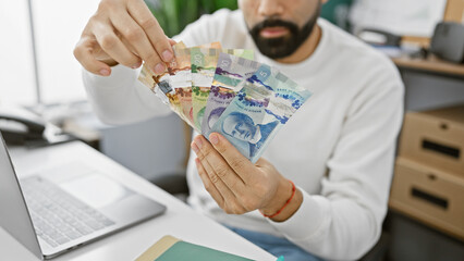 A young bearded man counts canadian currency at his modern office workplace, exemplifying financial work.