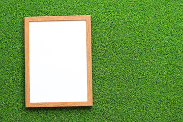 Empty frame for photo or text with a white sheet on a background of green grass. Artificial green grass leaf and simple wooden frame. Place for text