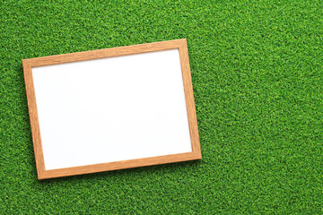 Empty frame for photo or text with a white sheet on a background of green grass. Artificial green grass leaf and simple wooden frame. Place for text
