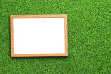 Empty frame for photo or text with a white sheet on a background of green grass. Artificial green grass leaf and simple wooden frame. Place for text