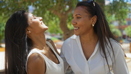Obraz premium Women smiling together outdoors in an urban park, showcasing love and friendship between a mother and daughter in a family setting.
