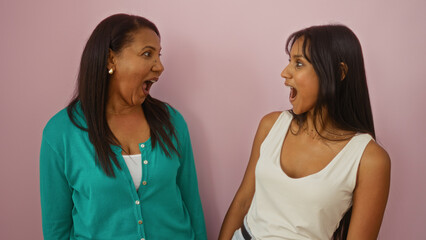 Mother and daughter sharing a surprised moment together over a pink background, showcasing love, family bond, and female friendship.