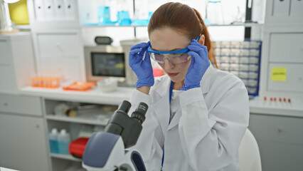 A young caucasian woman scientist analyzes samples using a microscope in a laboratory setting.