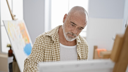 Fototapeta premium A senior man with grey beard engaged in painting indoors, concentrated on his creative hobby.