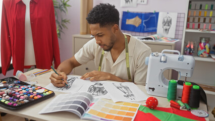A focused african american man sketches fashion designs in a colorful tailor shop with various tailoring tools.