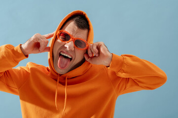 Fashionable cheerful man with cerebral palsy showing his tongue, wearing trendy orange color...