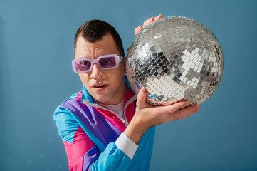 Naklejka premium Fashionable man with cerebral palsy wearing trendy purple color sunglasses, 80s style sport jacket, holding disco ball. Close up studio portrait. Copy, empty, blank space for text 