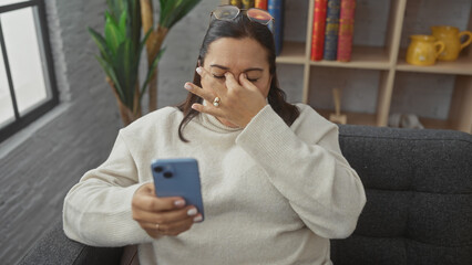 A concerned middle-aged hispanic woman using a smartphone in her modern living room, evoking themes...