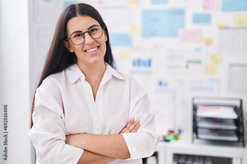 Sticker Young beautiful hispanic woman business worker smiling confident standing with arms crossed gesture at office