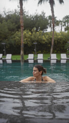Fototapeta premium A beautiful young hispanic woman enjoys a serene swim in a lush outdoor pool at a luxury bali resort.