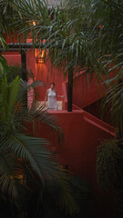 A young hispanic woman in white poses elegantly at a lush bali resort, blending tranquility with vibrant architecture.